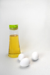 Vertical shot of three white eggs and a glass container with olive oil.