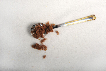 Pretty spoon with brown sugar placed diagonally across white surface.