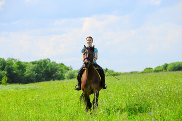 The Caucasian horsewoman is riding on the grass on the summer day.