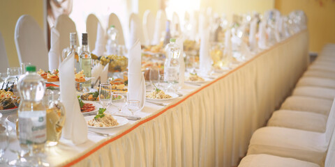 wedding festive table is decorated with glasses, plates and cutlery and covered with white tablecloth