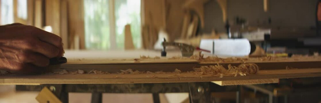 Caucasian male smoothing plywood a plane while building a canoe in his workshop. Boat making hobby, small business owner. Shot on RED Dragon