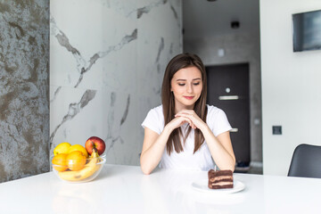 Diet. Dieting concept. Healthy Food. Beautiful Young Woman choosing between Fruits and Sweets