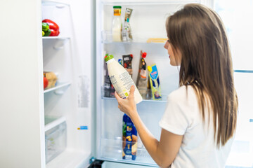 Woman chosen milk in opened refrigerator, cool new fridge full of tasty organic nutrition, female preparing to cook. Healthy eating concept
