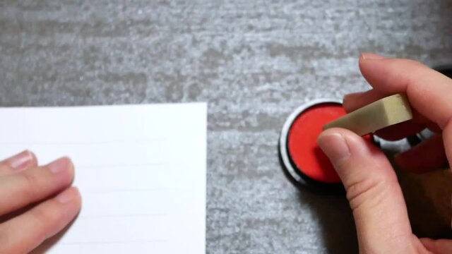 石で出来た篆刻のハンコを持つ。朱肉につけて印鑑を押す様子。
