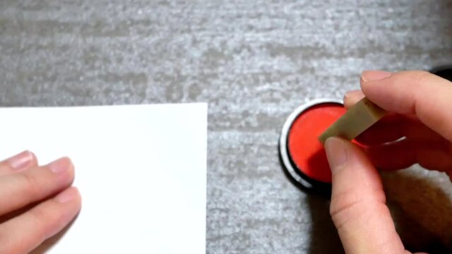 石で出来た篆刻のハンコを持つ。朱肉につけて印鑑を押す様子。