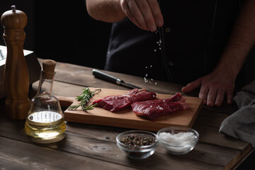 the chef sprinkles salt on the raw beef steak