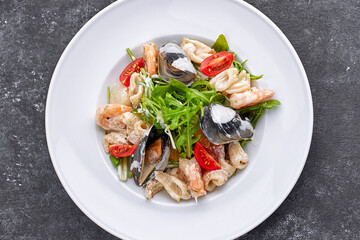 Seafood salad with mussels, squid, shrimp, on a round white plate, on a gray background
