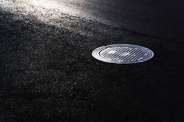 Sewer manhole on black asphalt. Beautiful road background.