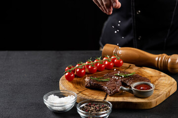 the chef sprinkles salt on the cooked beef steak on a wooden board