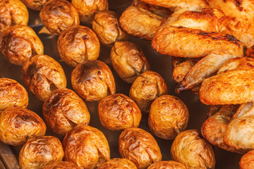 Closeup of baked jacket potatoes on a charcoal grill and chicken wings on a skewer. Fried vegetables and chicken to golden crust with spices on a street market. Food background