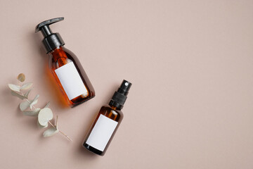 Obraz premium Amber glass cosmetic bottles and eucalyptus leaves on brown background. SPA bathroom natural cosmetic packaging mockup. Flat lay, top view.