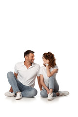 Fototapeta na wymiar happy couple in denim jeans sitting and looking at each other on white