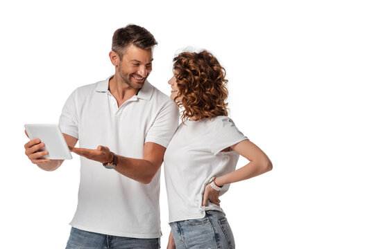 cheerful man pointing with hand at digital tablet and looking at woman isolated on white