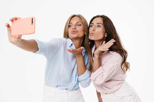 Image of two women blowing air kiss and taking selfie on cellphone