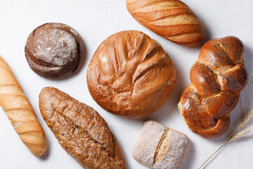 Variety of loaves of bread and buns on white background
