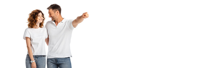 horizontal concept of happy man pointing with finger while looking at cheerful wife isolated on white