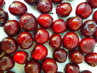 Scattered red cherry on a white background with drops of water.
