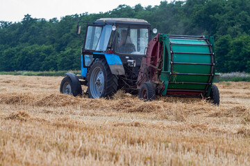 A tractor with a trailed bale making machine collects straw rolls in the field and makes round large bales