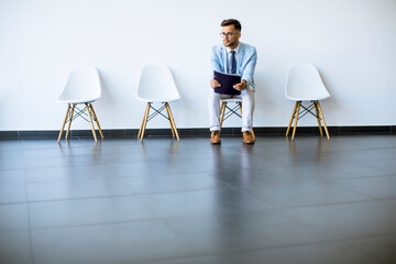 Young man sitting in the waiting room with a folder in hand before an interview