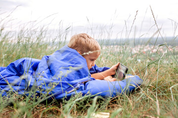 Local vacation. Boy in sleeping bag in the mountain chatting with friends via internet