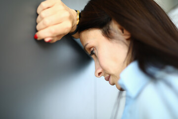 Sad woman is standing against wall with her elbow on her arm. Free psychological help concept