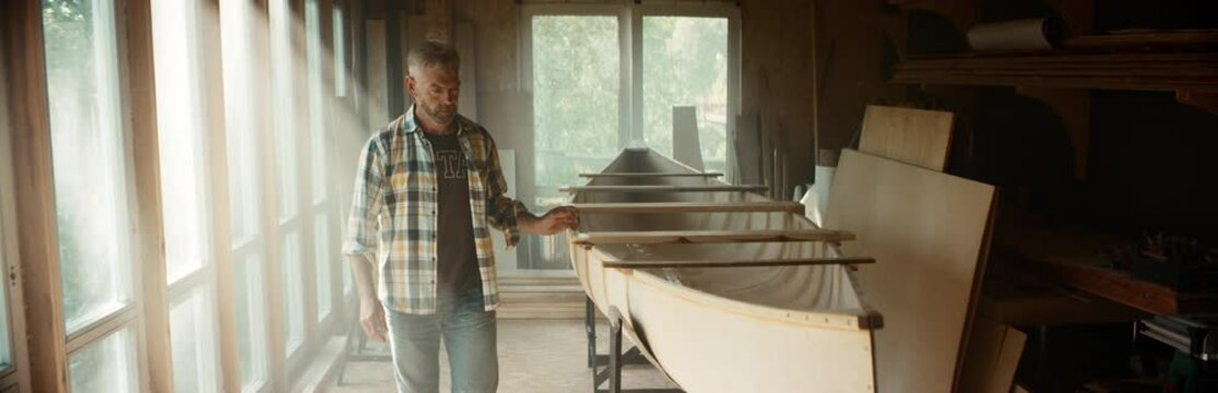 Portrait of Caucasian male touching a surface a canoe he is building in a workshop. Boat making hobby, small business owner. Shot on RED Dragon