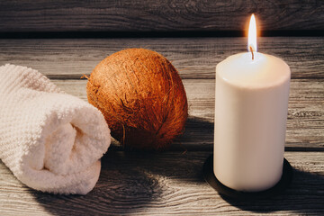 White rolled towel with coconut and burning candle on wooden table. Spa relaxtion procedure.