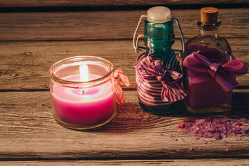 Spa setting with bottles of oil and burning candle. Pink sea salt. Old wooden background.