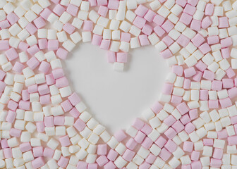 Cute pink and white mini small marshmallows arranged in a flat lay style to create negative space of a heart shape.  White background with space for copy text