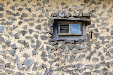 Old window on a retro house made of clay and wooden logs. Authentic farm series.