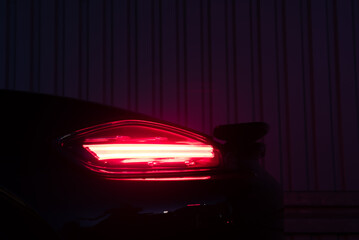 Heckleuchte /Bremsleuchte eines Sportwagens im Detail bei Nacht vor einer grauen Wand