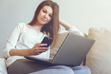 Woman lying on a sofa at home and holding in hand a smart phone.