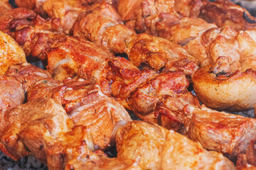 Closeup pork kebab on skewers cooked on a charcoal grill. Roasted meat with shallow depth of field. Large steaks of juicy fatty meat grilled on a street market. Food meat texture background.