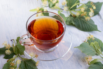 Glass cup of linden tea, and linden flowers on a white wooden table.