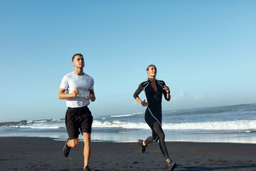 Beach. Woman And Man Running Along Coastline. Sport Couple In Fashion Sportswear On Outdoor Workout In Morning. Jogging Exercising Near Ocean On Summer Vacation As Part Of Active Lifestyle.