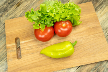 Fresh juicy vegetables peppers, tomatoes, cucumbers lettuce leaves with water drops are beautifully laid out on a wooden Board close-up. Vegetables are in the form of a funny face, top view