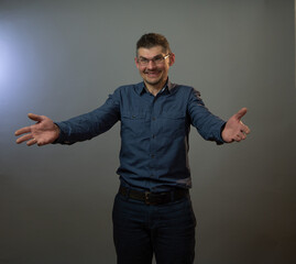 mature actor in glasses smiles posing with outstretched arms under electric light at studio audition close view