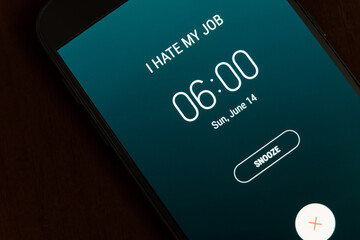 On a black smartphone, an alarm clock rings for 6 am with the inscription I hate my job close-up, background