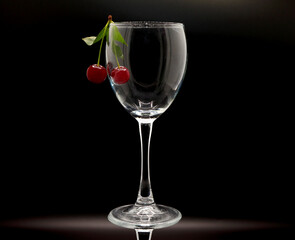 Pair of ripe cherries in an empty wine glass on a black background. Natural product. Natural color. Close-up.