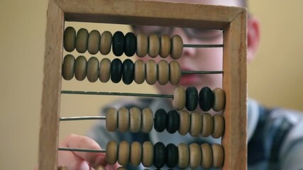 Caucasian boy wearing glasses of primary school age holding math abacus in front of him, doing his homework in mathematics. Selective focus, shallow depth of field