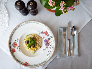 Risotto with snails and asparagus. The dish is decorated with pea microgreens. Sprinkled with grated cheese. White tablecloth, appliances and flowers are lying. Traditional Italian and French food. 