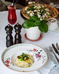 Risotto with snails and asparagus. The dish is decorated with pea microgreens.A pet is visible in the background.White tablecloth, appliances and flowers are lying. Traditional Italian and French food