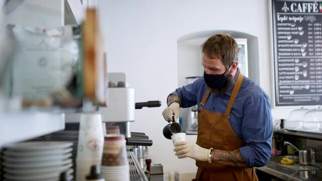 Man with face mask preparing coffee, shop open after lockdown quarantine.