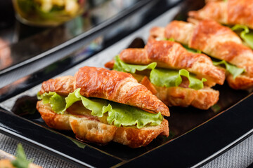 Mini croissant appetizer with cheese and prosciutto in plate on banquet table. Catering food, canape and snacks