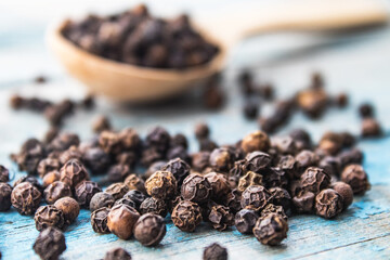 Dry black pepper in a wooden spoon near black pepper scattered on blue boards.