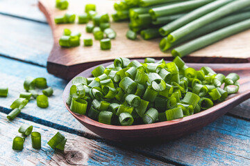 Sliced green onion rings in a wooden spoon on a background of old blue boards.