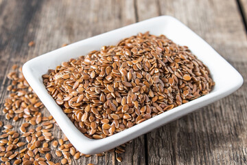 Flax seeds in a white bowl on a wooden table.