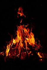Fototapeta na wymiar Burning wood at night. Bonfire in a tourist camp in nature in the mountains. Flames and fire sparks on a dark abstract background. Outdoor barbecue. The infernal element of fire. Fuel, power and energ