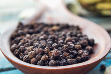 Black pepper in a large wooden spoon on a background of blue boards.