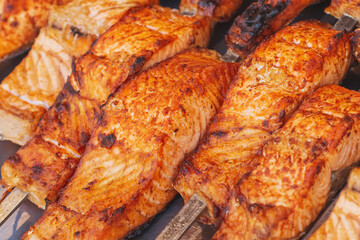 Huge delicious appetizing mouth-watering grilled salmon steaks on a street market counter. Red fish on metal skewers cooked on a charcoal grill. Fried red fish with selective focus.